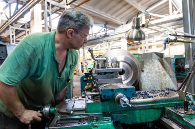 İşçi, bir adam bir makine üzerinde metal ürünler işler. Üretim çalışmalarında dönüm