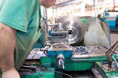 İşçi, bir adam bir makine üzerinde metal ürünler işler. Üretim çalışmalarında dönüm