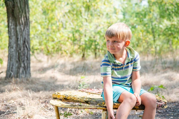 男孩坐在一张旧板凳上 在一个废弃的公园里 带着悲伤的表情环顾四周 — 图库照片
