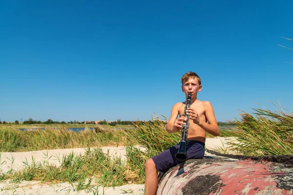 Chłopiec Bawi Się Czarny Klarnet Siedząc Starej Drewnianej Łodzi Plaży — Zdjęcie stockowe