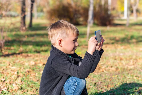 Küçük Bir Çocuk Parkta Telefonda Güneşli Bir Günde Fotoğraf Çeker — Stok fotoğraf