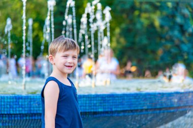 Bir oğlan mavi tişört çeşme arka plan üzerinde duruyor.