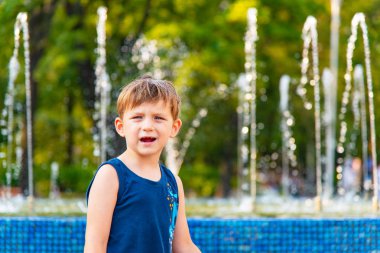 Bir oğlan mavi tişört çeşme arka plan üzerinde duruyor.