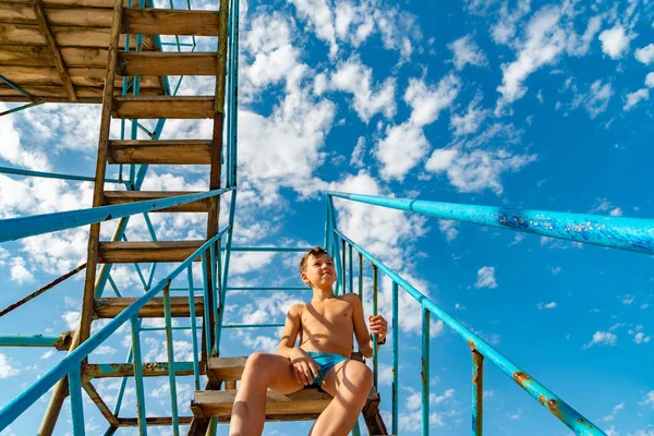 Rapaz Calções Banho Senta Nas Escadas Praia Num Cenário Nuvens — Fotografia de Stock