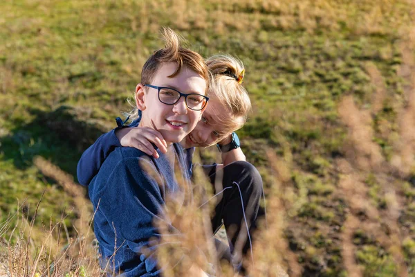 A boy with a girl are sitting on a cliff, two friends, a brother and sister are sitting in an embrace and look into the camera through the back