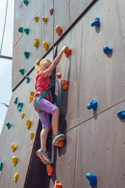 Neşeli ve mutlu bir kız sarışın, bir emanet ip ile kameraya bir yapay kaya ve görünüyor en tepeye tırmanıyor kaya tırmanışı devreye girer