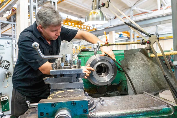 A worker, a man in a black shirt and safety glasses, checks the part for suitability for use in equipment. Turning work in production