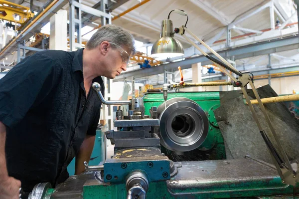 Worker, a man processes metal products on a machine. Turning work in production