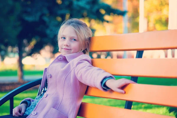 Dziewczyna Różowym Płaszczu Siedzi Żółtej Ławce Parku — Zdjęcie stockowe