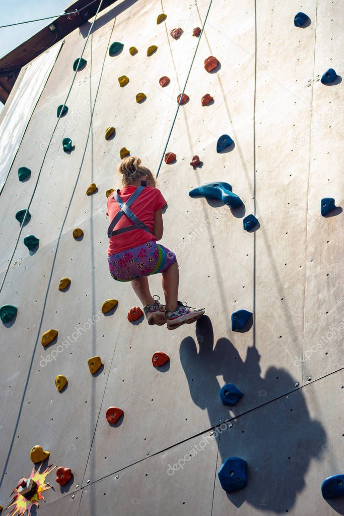 The girl descends from an artificial rock with the help of a safety rope, is engaged in rock-climbing