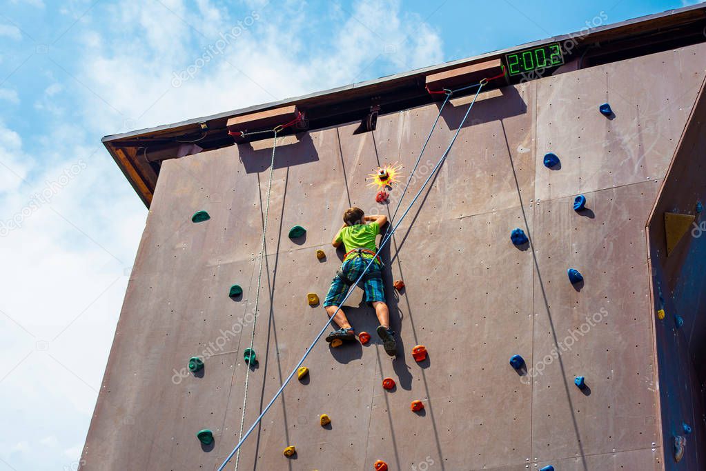 The guy the teenager climbs to the top of the artificial rock, is engaged in rock climbing