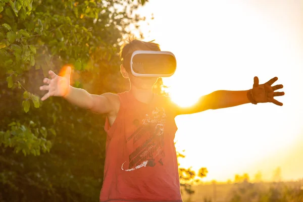 A boy outdoors in a forest in a VR helmet. Virtual reality in nature with sunlight