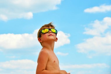Küçük bir çocuk bulutlu gökyüzü gözlük ile görünüyor. Bulutlar cam yansıtılır. Mavi gökyüzüne karşı sarı gözlük.