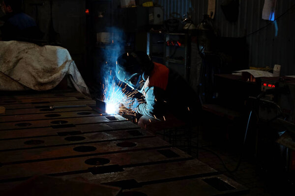 The welding welder is engaged in the manufacture of parts welding with sparks.