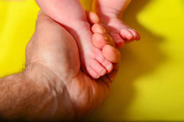 Babybeine Auf Gelbem Hintergrund Papa Hält Die Kleinen Beine Eines — Stockfoto