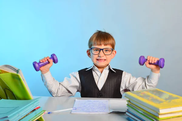 Den lilla skolpojke bedriver hantlar bland anteckningsböcker och läroböcker vid sitt skrivbord på skolan i klassrummet. — Stockfoto