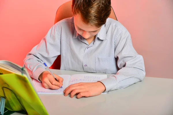 En student med glasögon gör läxor, skola läxor vid ett skrivbord med läroböcker. Studenten förbereder sig för tentor — Stockfoto