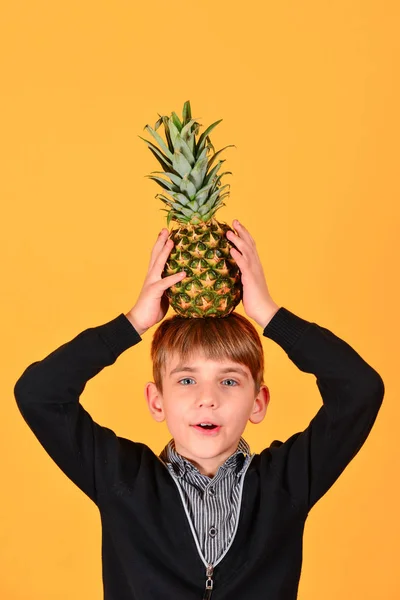 Çocuğun kafasına sarı bir arka plan üzerinde bir ananas tutar — Stok fotoğraf