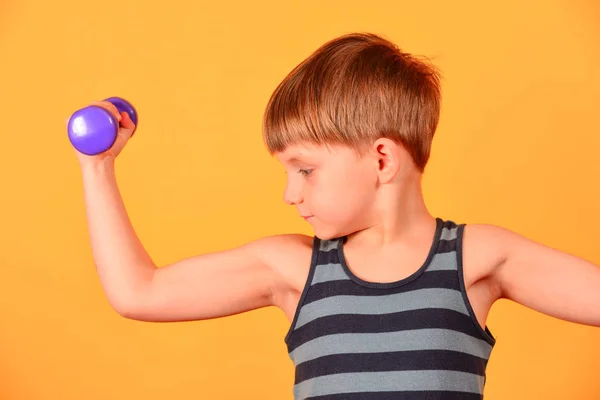 Хлопчик з фіолетовими гантелями входить у спорт і робить фізичні вправи в студії на жовтому тлі — стокове фото