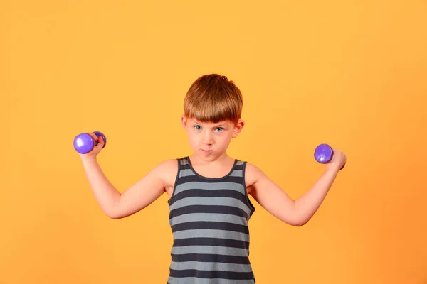 Um menino com halteres roxos entra para esportes e faz exercícios físicos no estúdio em um fundo amarelo — Fotografia de Stock