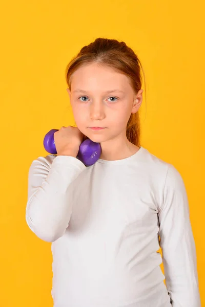 Genç ve atletik kız sarı bir arka plan üzerinde dumbbells ile fiziksel egzersizler yapıyor — Stok fotoğraf