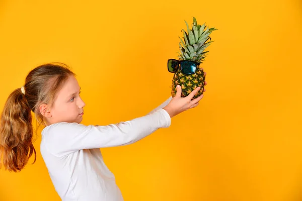 La ragazza indossava occhiali da sole su un ananas e lo guarda — Foto Stock