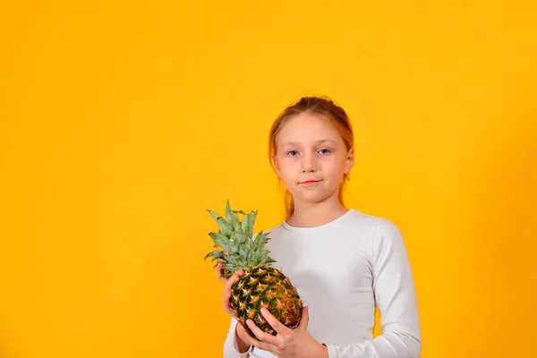 Roztomilá dívka v bílém drží v ruce, na žlutém pozadí ananas — Stock fotografie