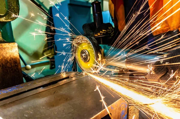 Pracovník škrty obrobku s elektrickou brusku, mnoho jiskry létají do stran. — Stock fotografie