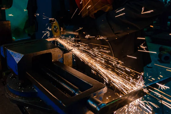 The worker cuts the workpiece with an electric grinder, many sparks fly sideways. — Stock Photo, Image