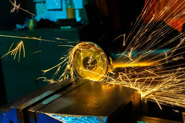 The worker cuts the workpiece with an electric grinder, many sparks fly sideways.