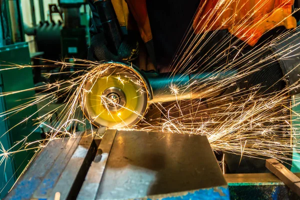 Pracovník škrty obrobku s elektrickou brusku, mnoho jiskry létají do stran. — Stock fotografie