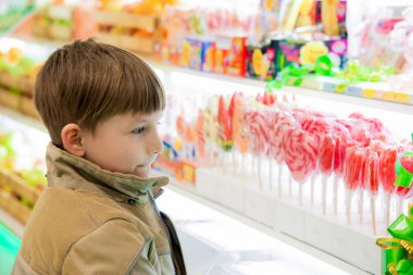 Bir çocuk tatlılar ve tatlılar bir alışveriş merkezinde bir dükkan pencere üzerinde arıyor.