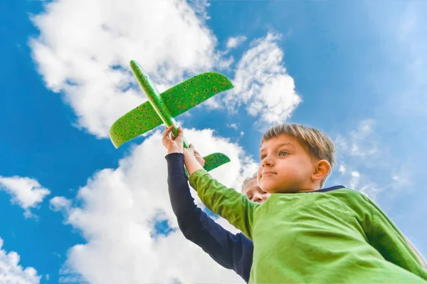 Τα παιδιά κρατούν ένα πράσινο αεροπλάνο στα χέρια τους εναντίον ενός γαλάζιου ουρανού στα σύννεφα. έννοια του τουρισμού, των ταξιδιών και της ελευθερίας — Φωτογραφία Αρχείου