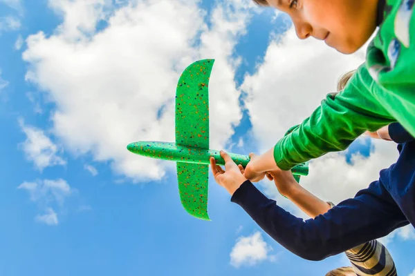 Les enfants tiennent un avion vert dans leurs mains contre un ciel bleu dans les nuages ; concept de tourisme, de voyage et de liberté — Photo