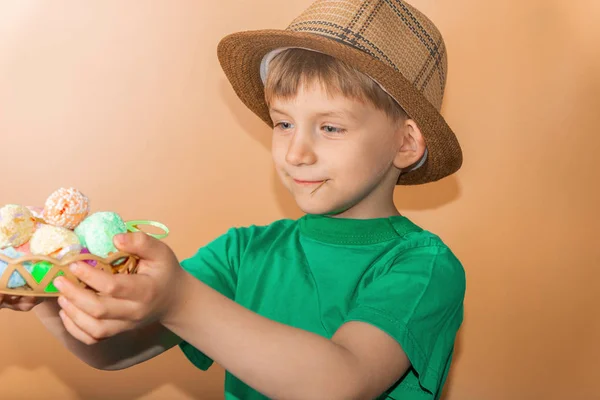 Un niño con un sombrero de paja sostiene huevos de Pascua pintados en su mano . —  Fotos de Stock