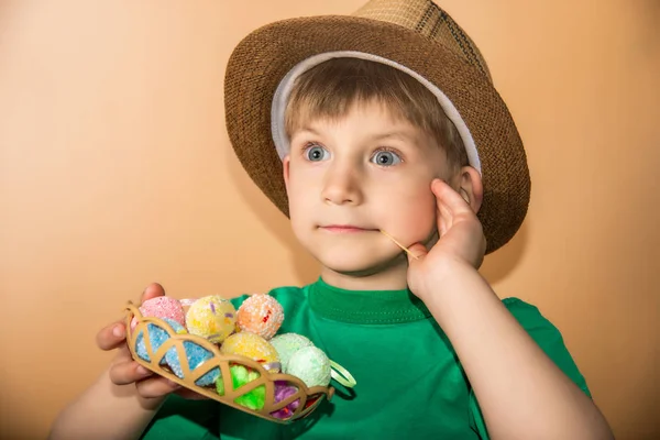 Un niño con sombrero de paja sostiene huevos de Pascua en una canasta . —  Fotos de Stock