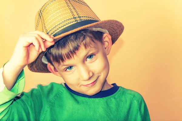 Un niño con sombrero de paja y una camiseta verde sosteniendo un sombrero en señal de saludo . —  Fotos de Stock