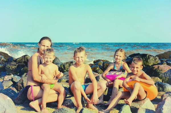 Mama z dziećmi na morzu na morzu na plaży, woda bije na kamienie. Stonowane rocznika zdjęcie. — Zdjęcie stockowe