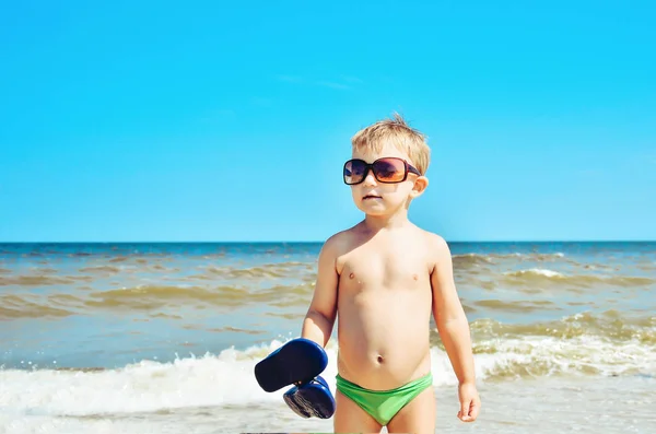 Chłopiec w okularach stoi na plaży nad morzem. — Zdjęcie stockowe