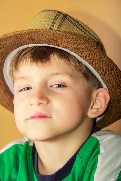 Um menino orgulhoso e ganancioso em um chapéu de palha com uma expressão facial arrogante olha para a câmera em um fundo amarelo . — Fotografia de Stock