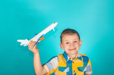 Çocuk elinde bir oyuncak uçak tutar ve parlak renkli gömlek, mavi bir arka plan üzerinde stüdyoda fotoğraf gülümsüyor.