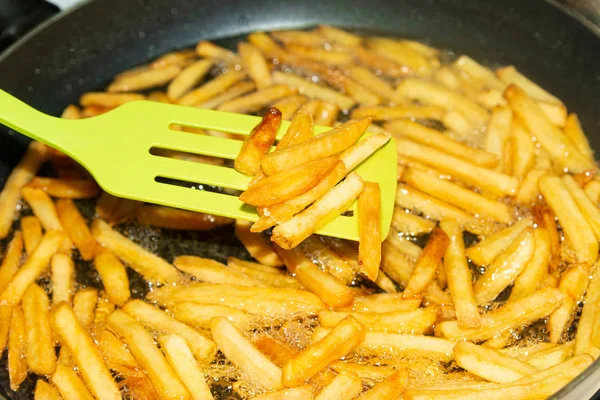 Un cocinero mezcla una espátula con papas fritas en una sartén en aceite de girasol . —  Fotos de Stock