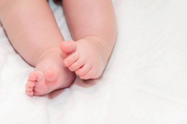 Ayaklar beyaz bir yatak örtüsü üzerinde yeni doğan bebek. Küçük bebek bacakları yakın.