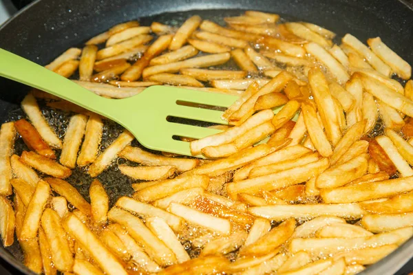 Un cocinero mezcla una espátula con papas fritas en una sartén en aceite de girasol . —  Fotos de Stock