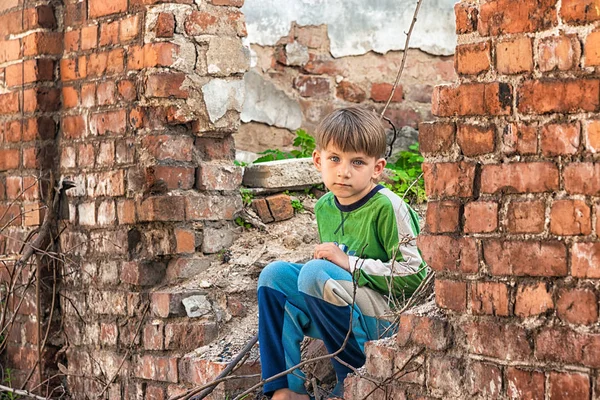 Pobre e infeliz niño huérfano, sentado en las ruinas y ruinas de un edificio destruido. Foto escenificada . —  Fotos de Stock