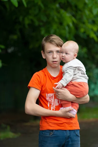 Όμορφος και ενήλικος αγόρι που κρατά ένα μικρό παιδί στην αγκαλιά του, πορτρέτο μιας νεαρής ευτυχης οικογένειας. — Φωτογραφία Αρχείου