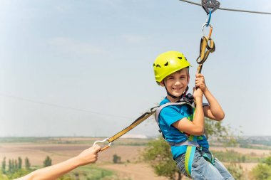Koruyucu bir kask ve sigorta giymiş bir çocuk, ip aşağı gider, koruyucu bir kablo tutarak iner.
