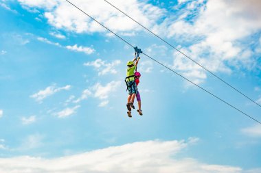 Erkek ve kız kardeş aşırı bir parkta ipten aşağı inerler. Bloklu insanlar halata tutunup aşağı yuvarlanıyorlar..