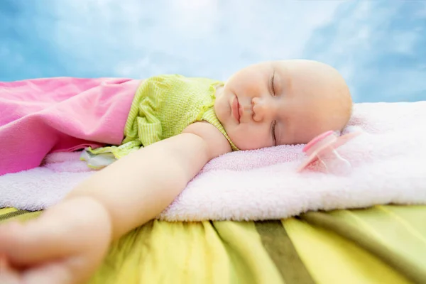 Das Kind schläft auf der Straße in einem Kinderhandtuch, gegen den Himmel, die Brustwarze liegt in der Nähe. Weitwinkelbild. — Stockfoto