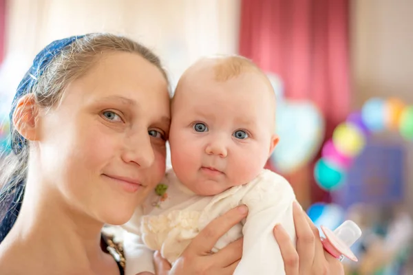 Glückliche und freudige Mutter nimmt das Baby in den Arm, lächelt und blickt in die Kamera. — Stockfoto